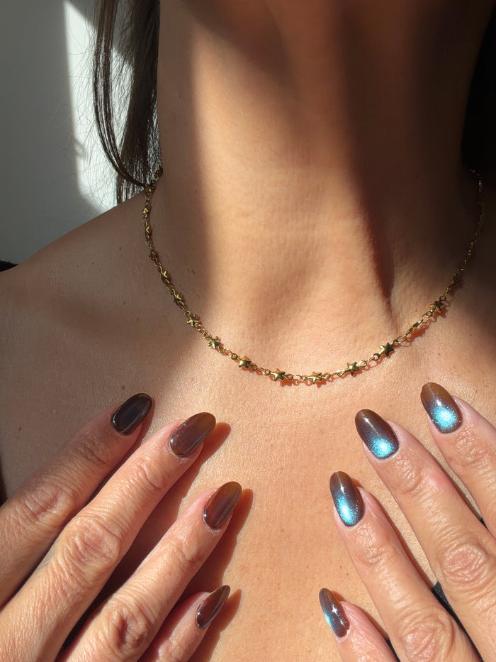A stainless steel gold PVD star chain choker necklace, hanging on a model’s neck 